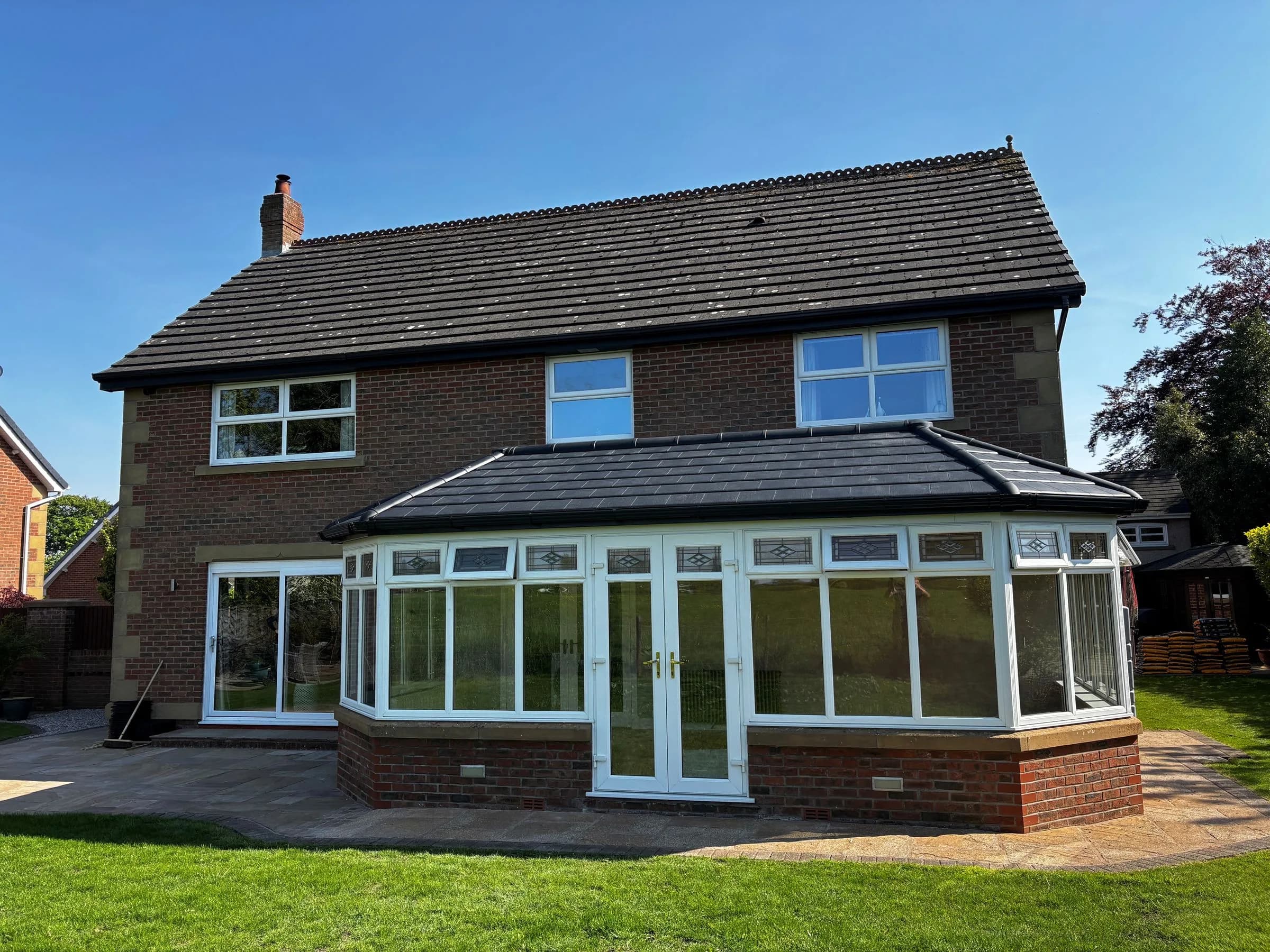 SupaLite lightweight tiled conservatory roof in dark grey tiles on a brick house, seen from the lawn.