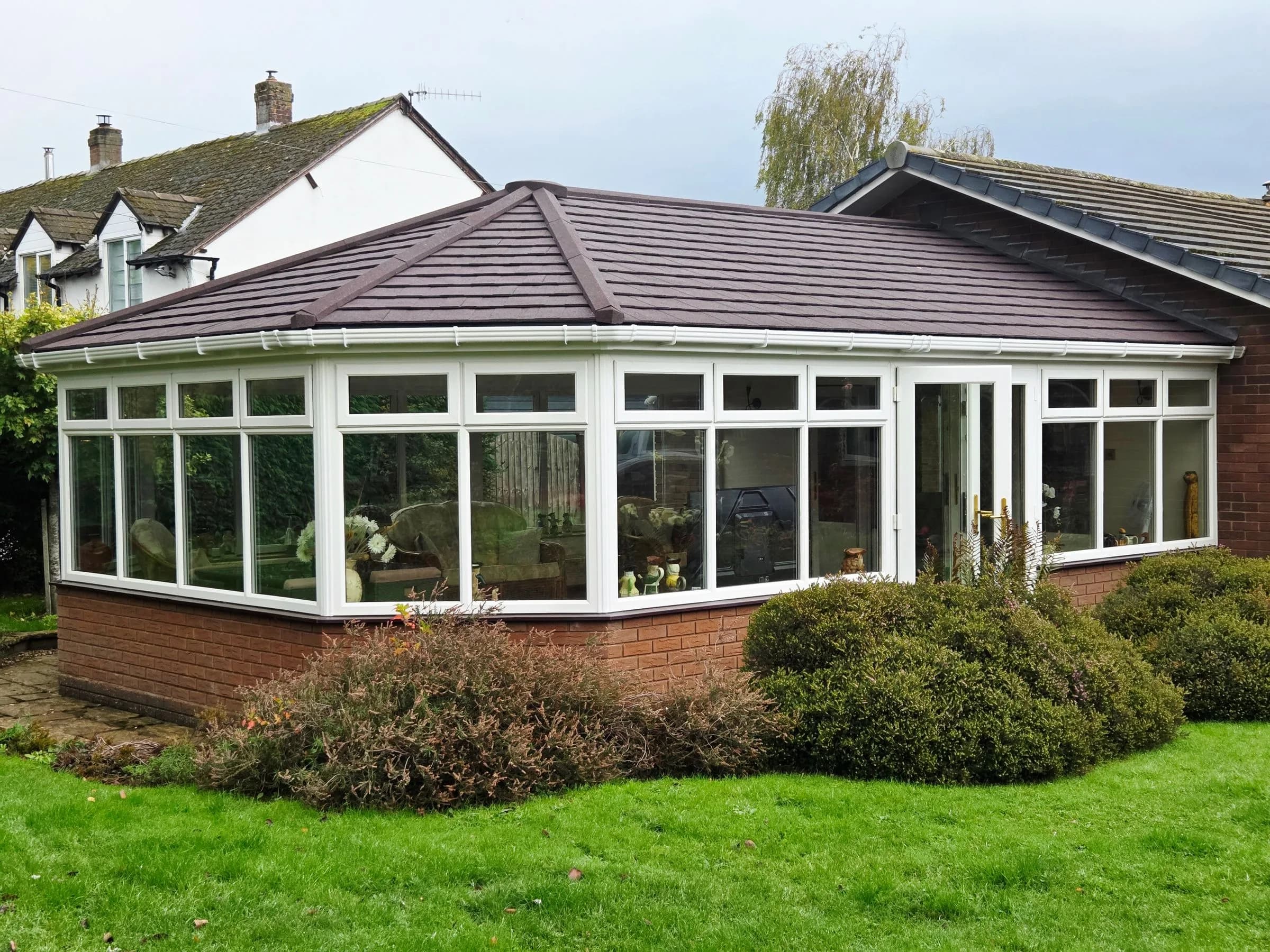 SupaLite lightweight tiled conservatory roof in brown tiles on a wide conservatory against a bungalow, seen from the garden.