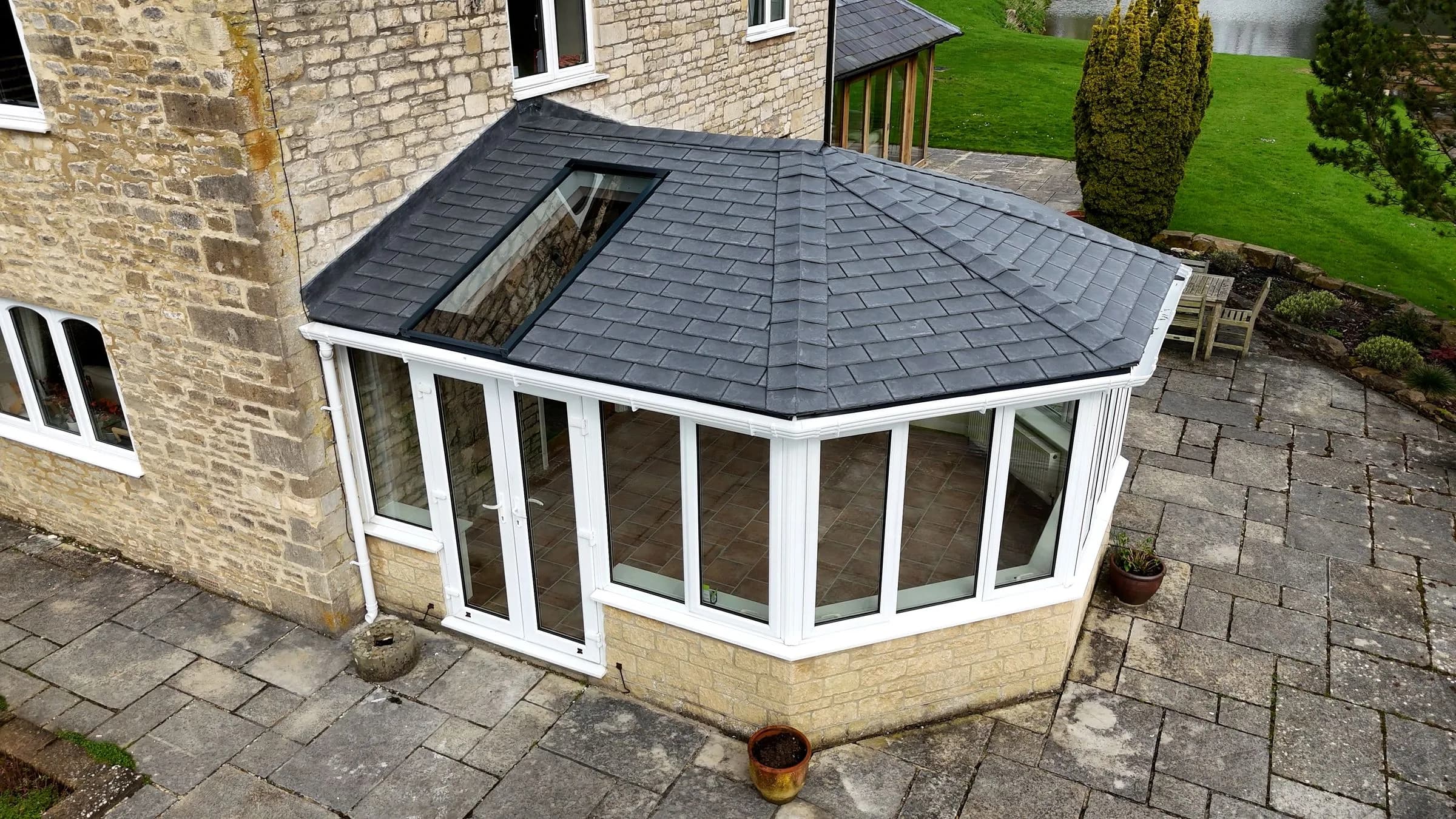 SupaLite lightweight tiled conservatory roof in grey tiles against a stone house, with a roof window set into the slope.