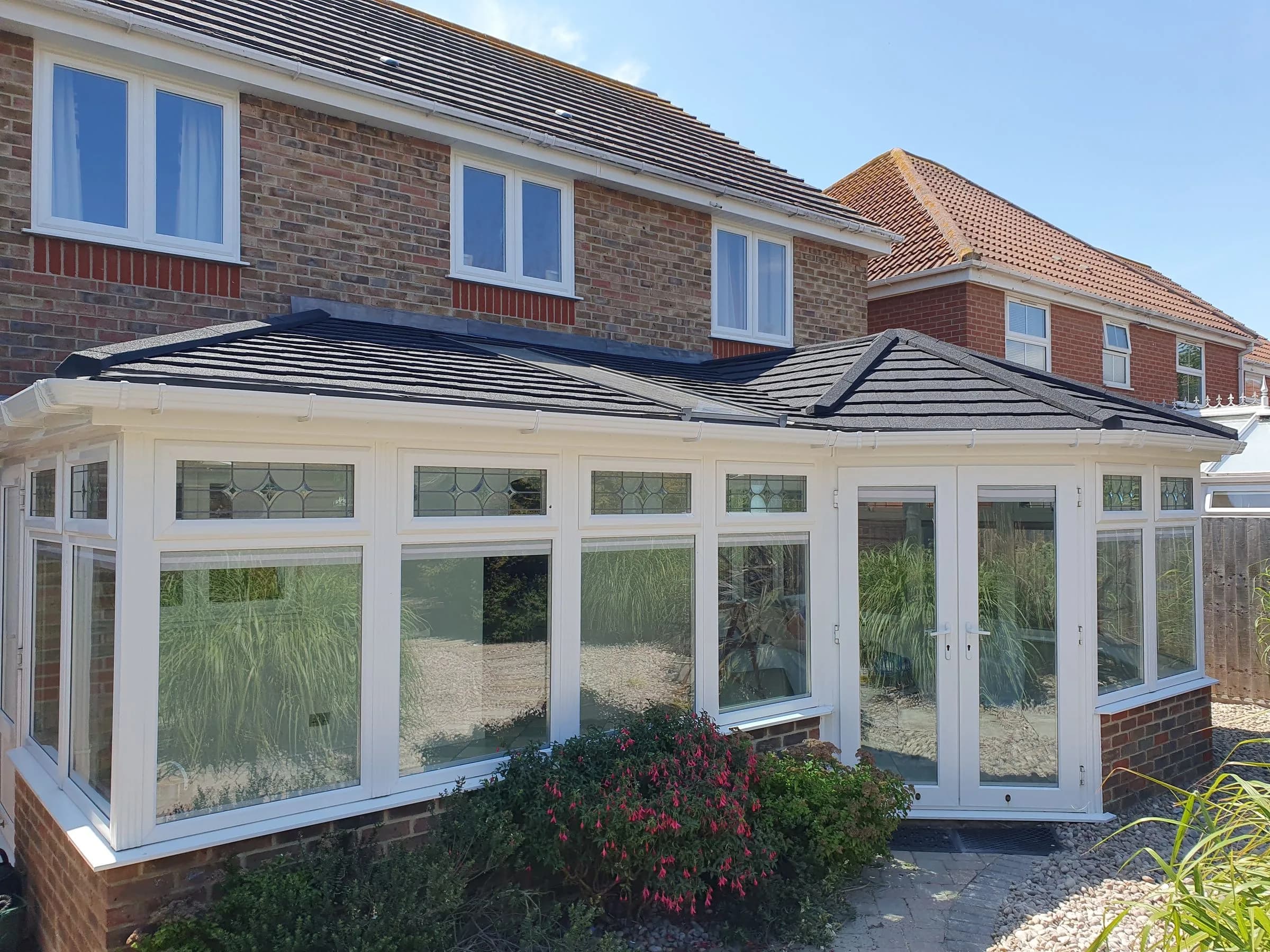 SupaLite lightweight tiled conservatory roof in dark grey tiles on a large white conservatory, seen from the garden.