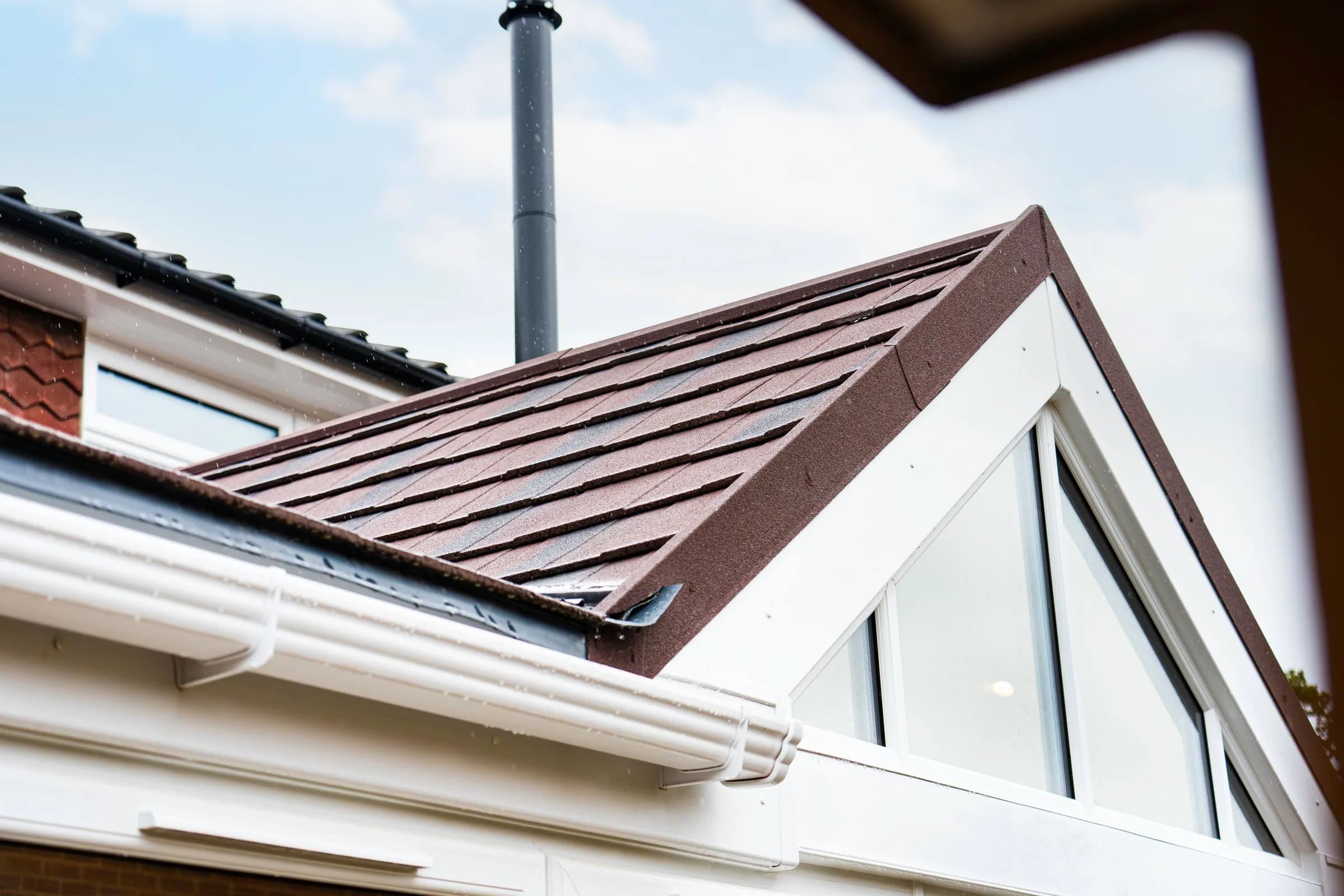 The gable end and ridge of a WarmerRoof conservatory roof in terracotta tiles, close enough to read the tile courses.