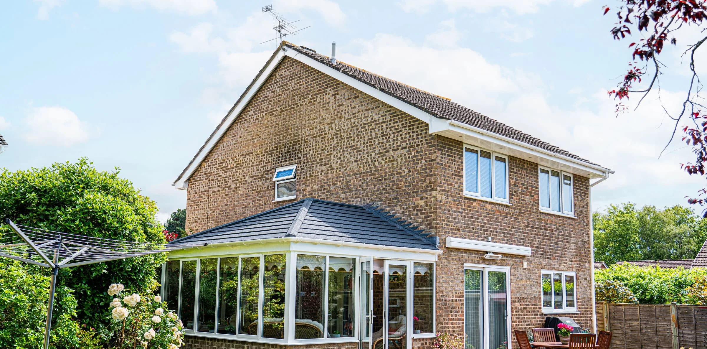 WarmerRoof tiled conservatory roof in dark slate-effect tiles, across the back of a brick house, seen from the garden.