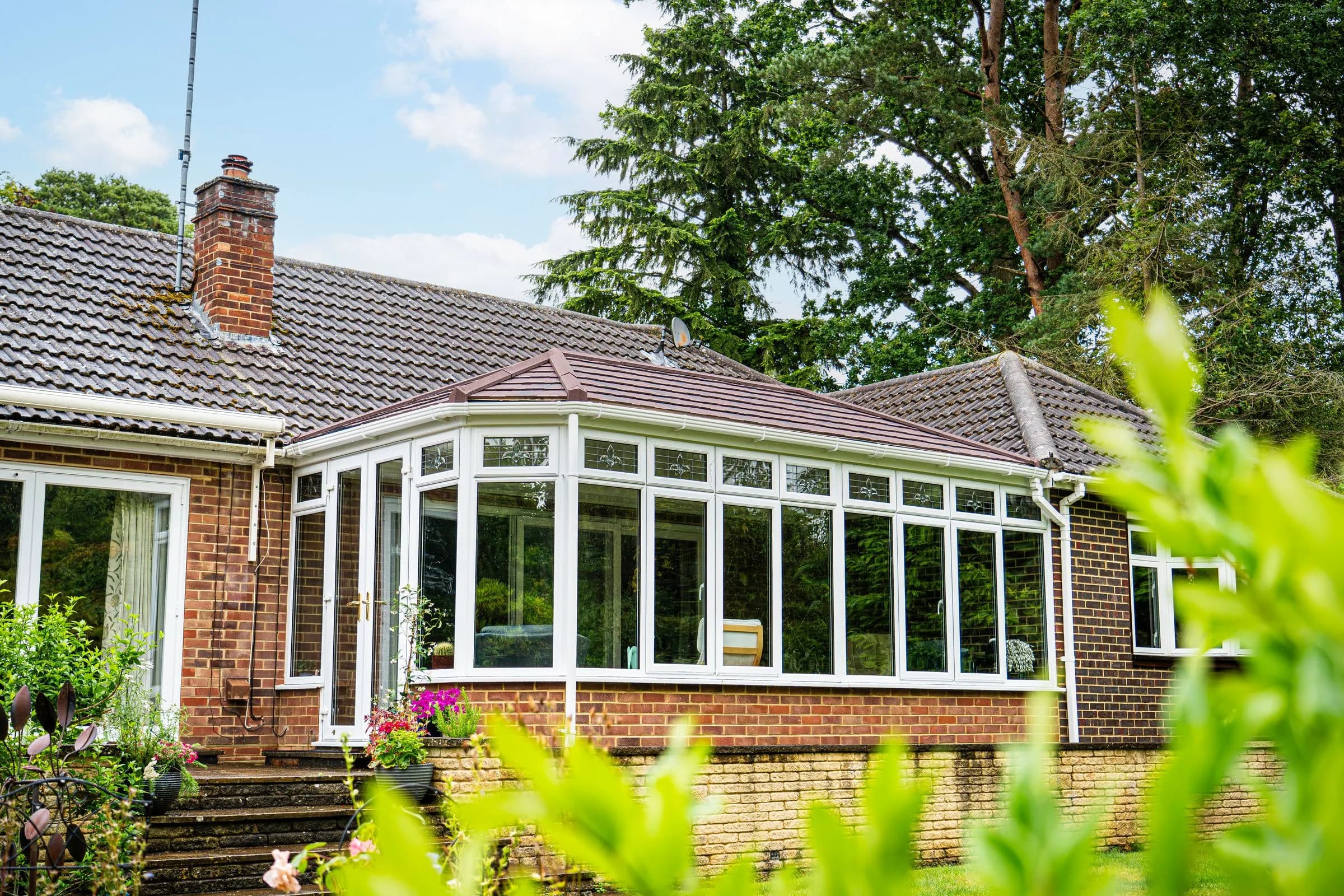 WarmerRoof tiled conservatory roof in terracotta tiles on a long conservatory against a bungalow, seen from the garden.